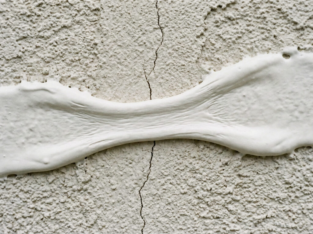A close-up view of a thick elastomeric exterior coating stretching to cover
and seal a hairline crack in a stucco wall.