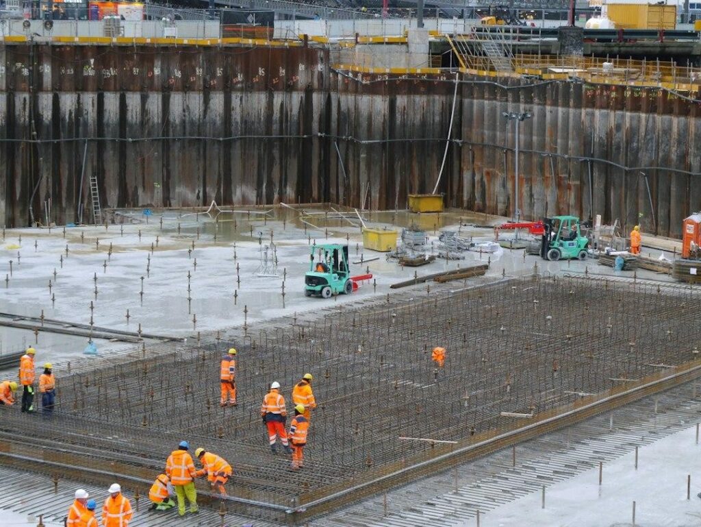 Construction workers in high-visibility vests laying steel reinforcing mesh for a large concrete slab